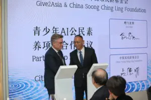 Head of China Soong Ching Ling Foundation and CEO of Give2Asia shake hands in front of audience at Give2Asia Anniversary event. 