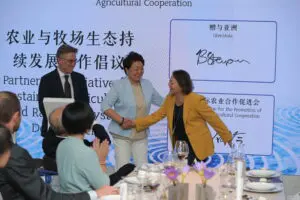 Head of CAPIAC with Give2Asia CEO and China Chief Representative shake hands in front of audience at Give2Asia Anniversary event. 