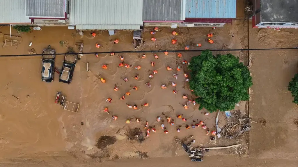 aerial shot of people wading in brown flood waters raking and shoveling debris